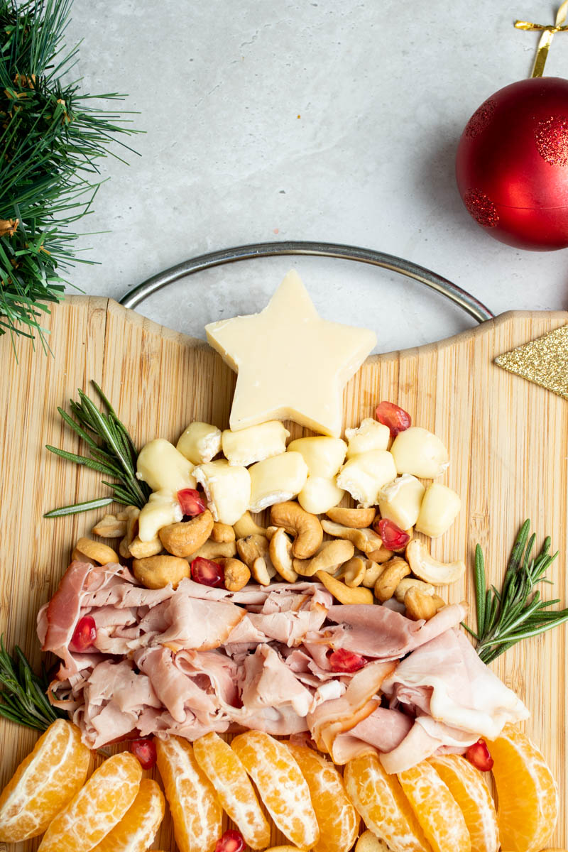 Cheeses, meats, fruits and nuts on a wooden cutting board, to form a Christmas-theme festive charcuterie board.