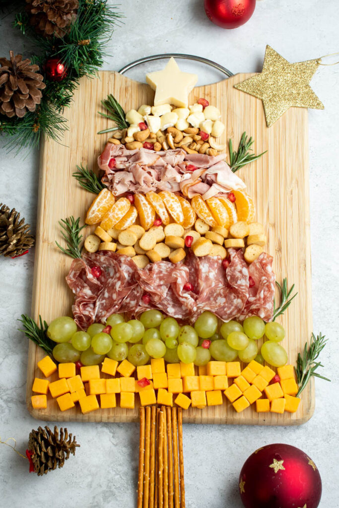 Cheeses, meats, fruits and nuts on a wooden cutting board, to form a Christmas-theme festive charcuterie board.
