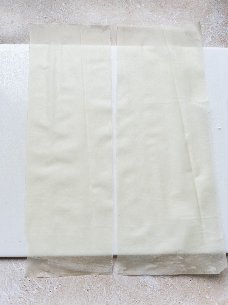 Two strips of fillo pastry sheets on a white cutting board.