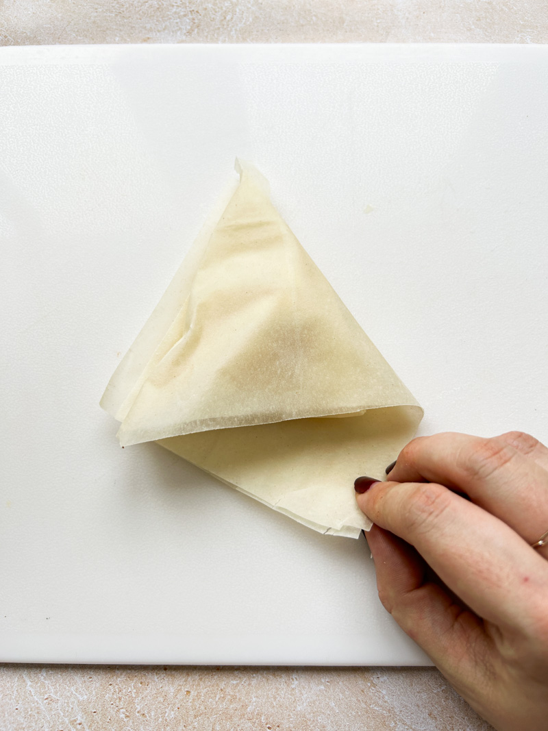 One hand places the excess fillo pastry sheet inside the triangle.