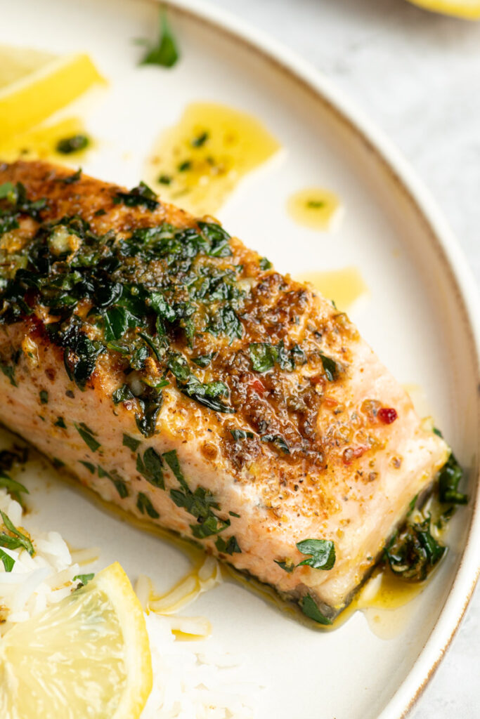 Grilled salmon fillet with herb butter in a white plate.