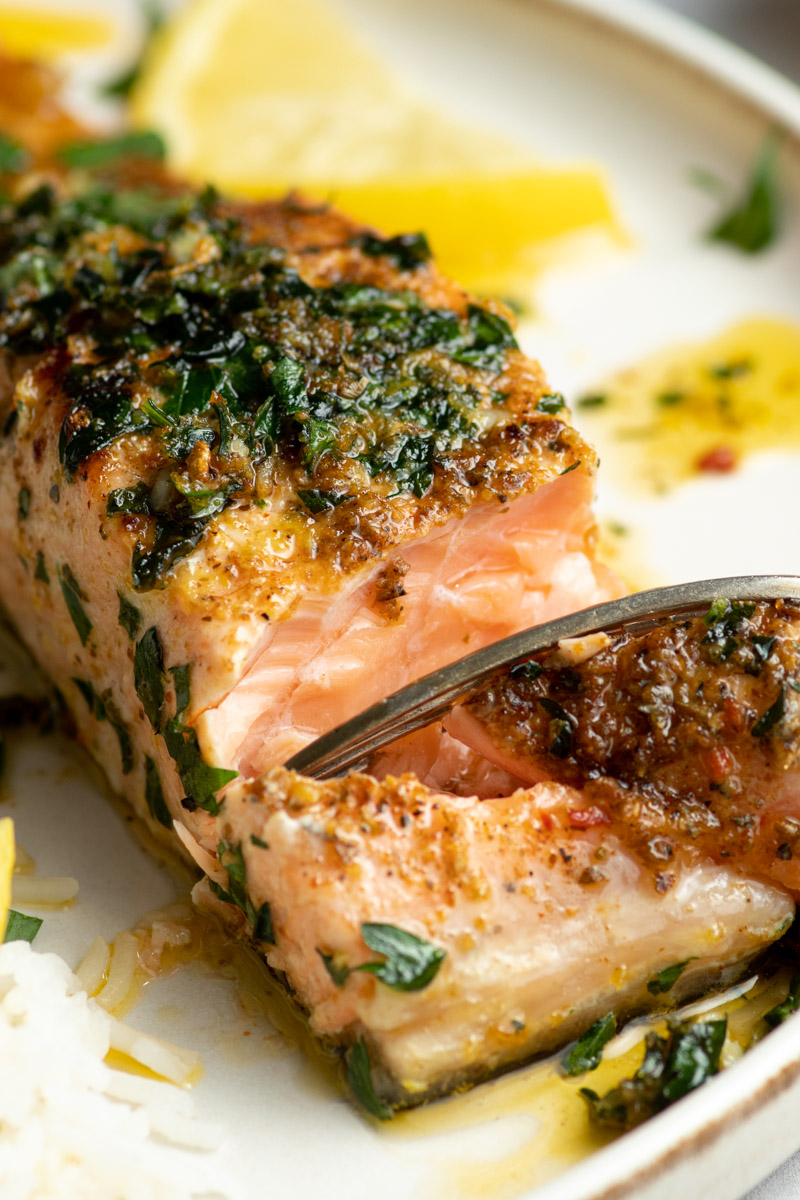 Une fourchette coupe le filet de saumon, montrant la chair d'un filet de saumon parfaitement cuit.