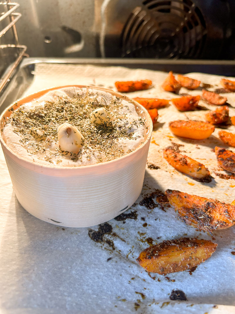 Vacherin Mont d'Or cooking in the oven, next to the potatoes.