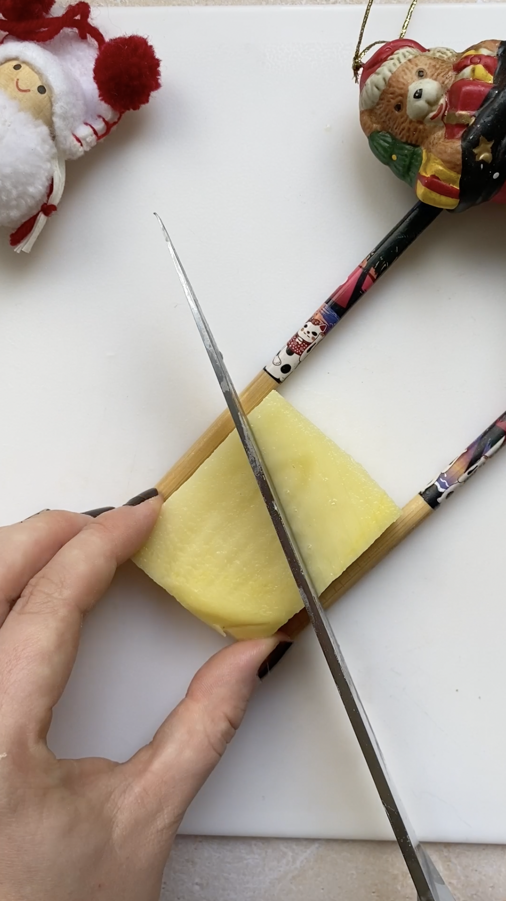 A hand holding a knife, cutting a potato in diagonal lines.