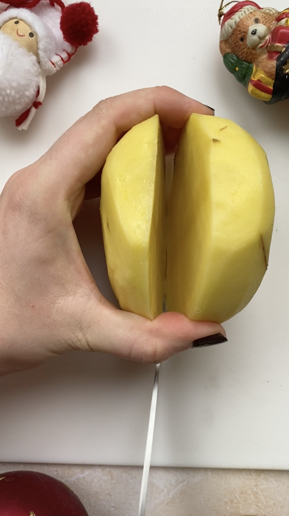 A hand holding a knife, cutting a potato in slices.