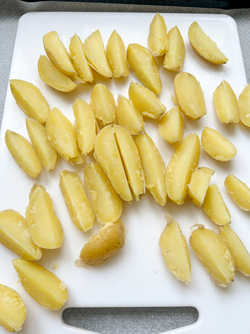 Pommes de terre coupées en quartiers, sur une planche à découper blanche.