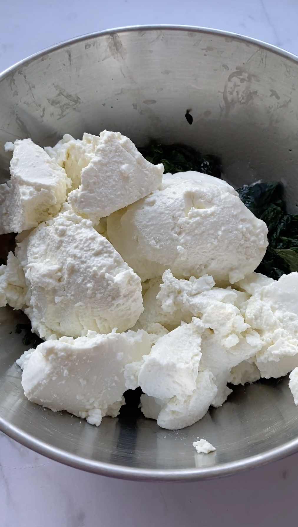 Ricotta cheese in a grey bowl with cooked spinach.