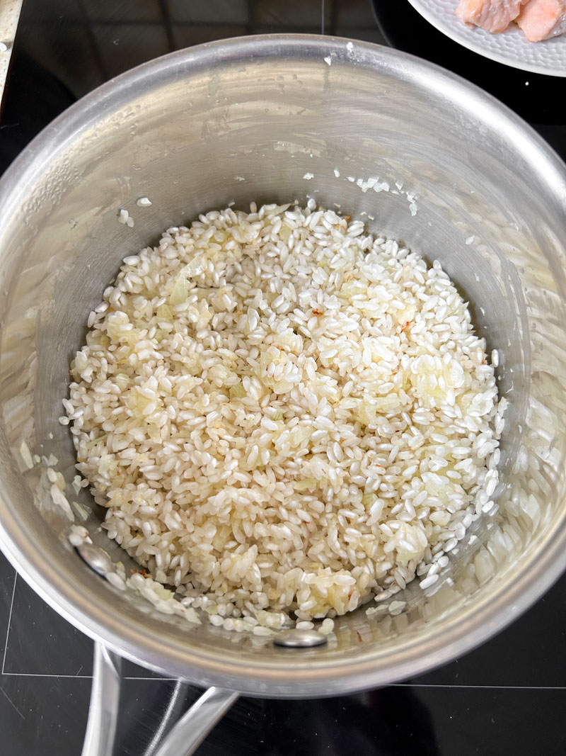 Risotto rice added to the saucepan of minced garlic and onion.