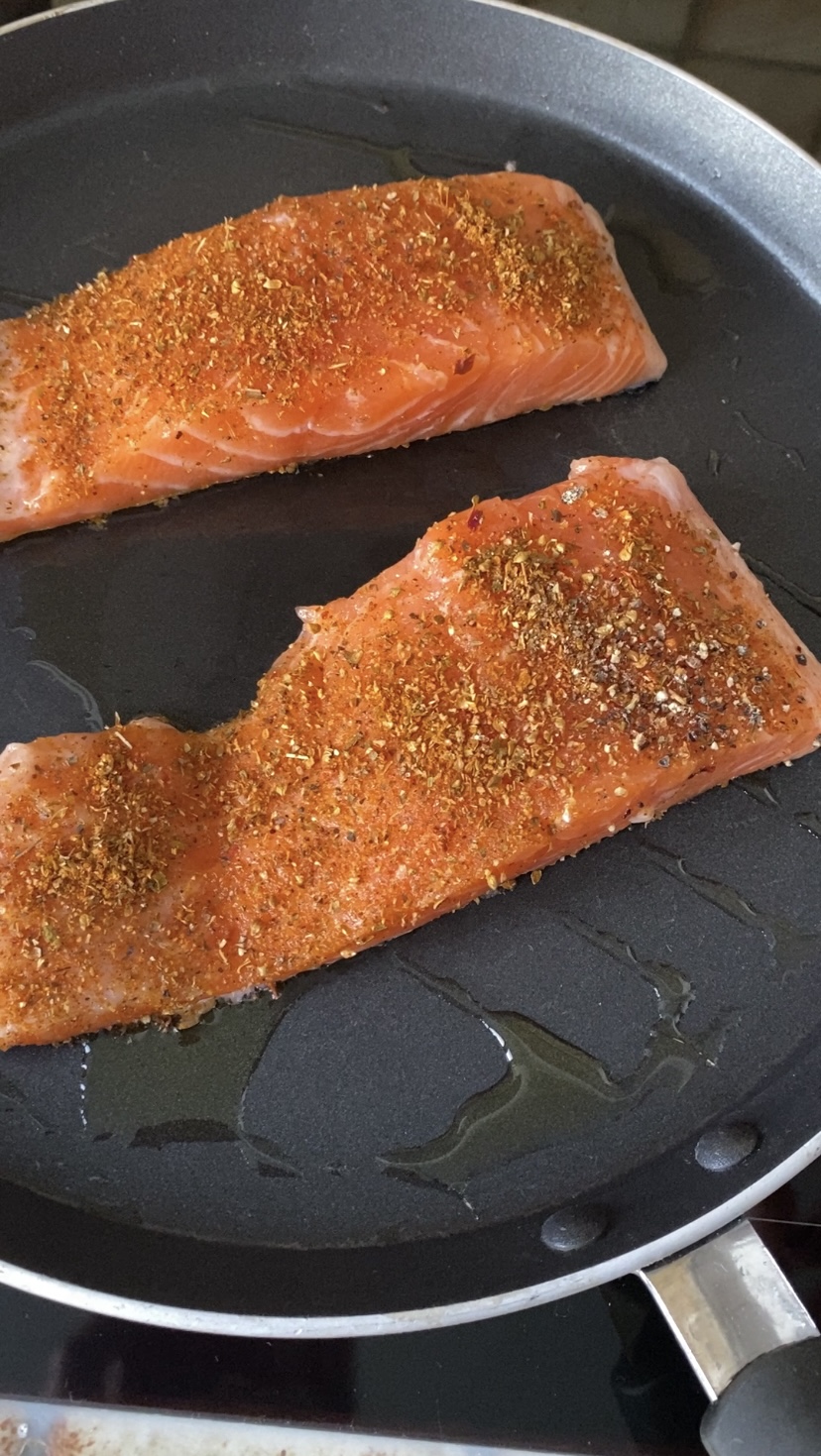 Salmon fillets cooking in a frying pan with olive oil.