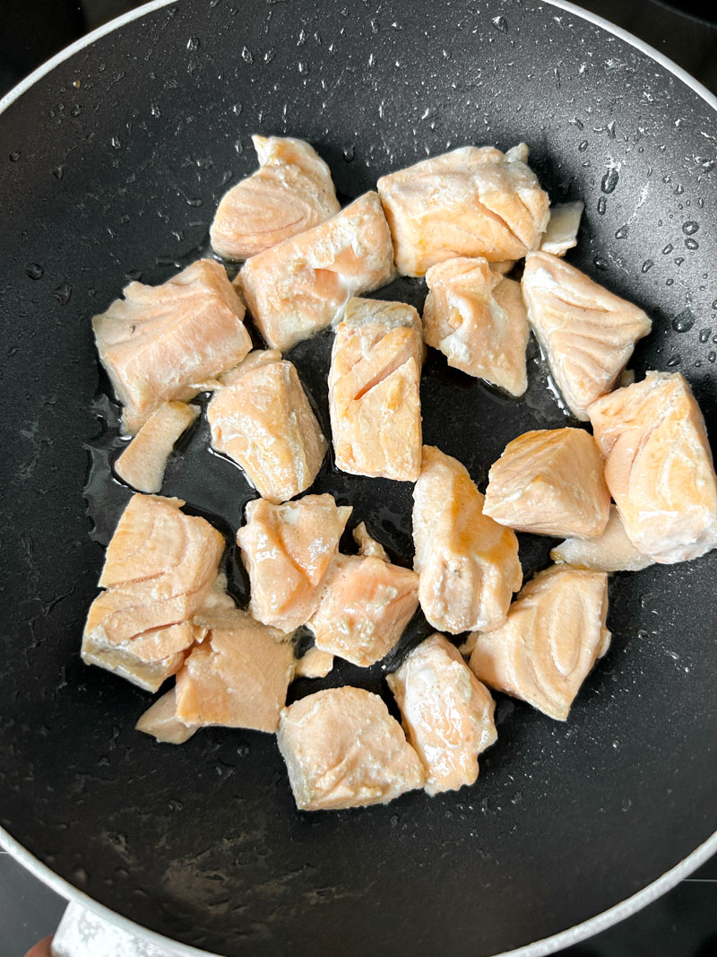 Salmon cubes, cooked, in a frying pan.
