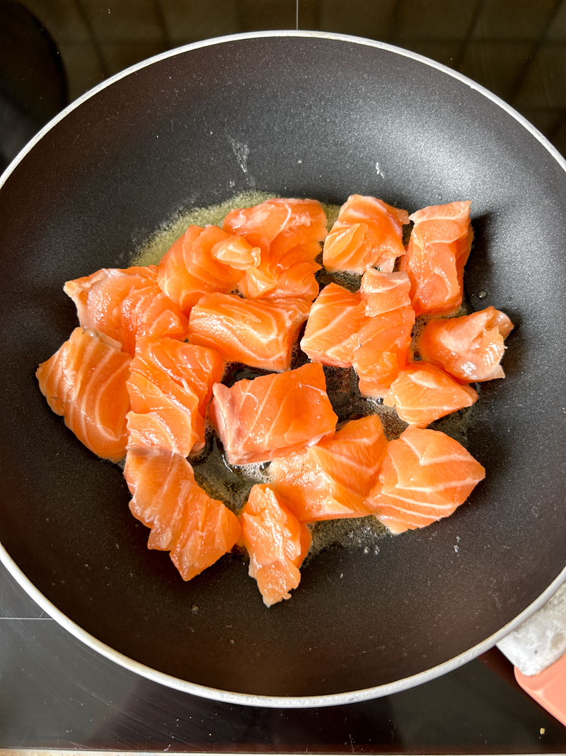 Salmon cubes cooking in a frying pan with melted butter.
