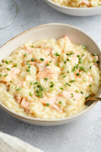 Creamy salmon risotto with chives in two beige bowls, with a fork.