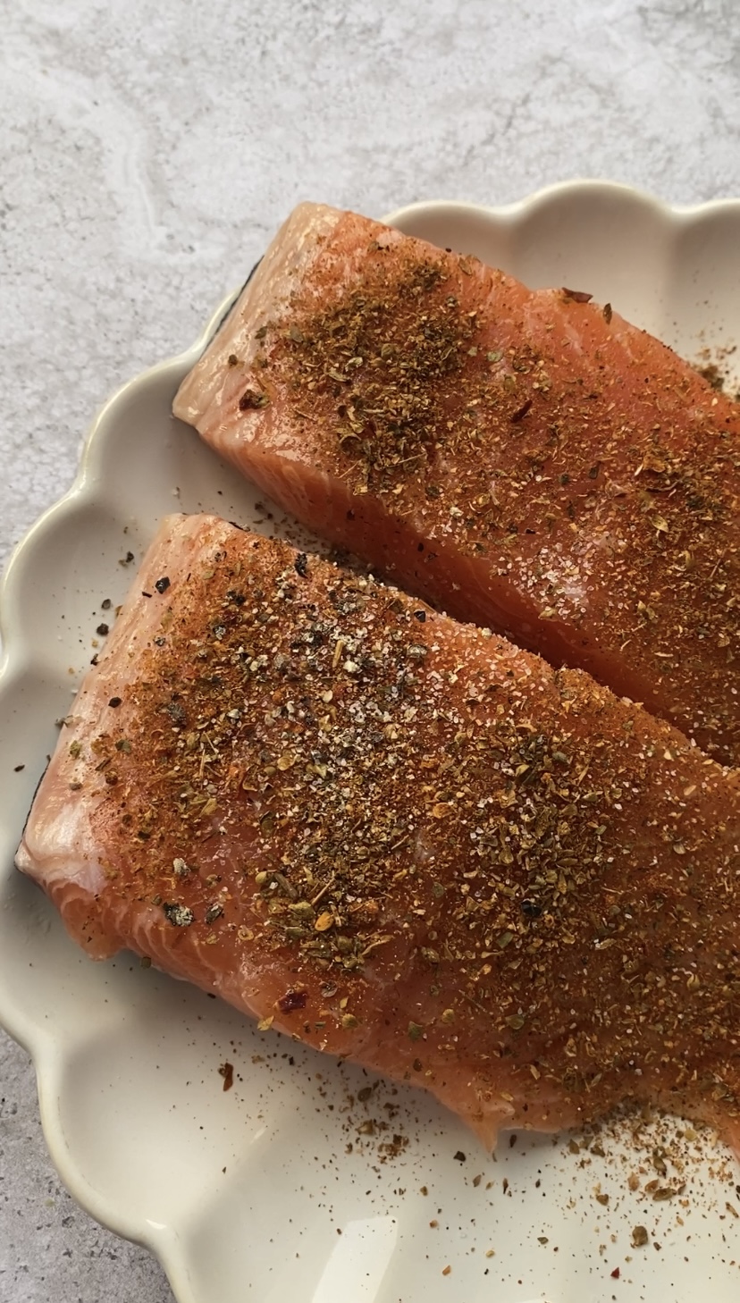 Salmon fillets in a white plate, seasoned with salt, black pepper and Italian seasoning.