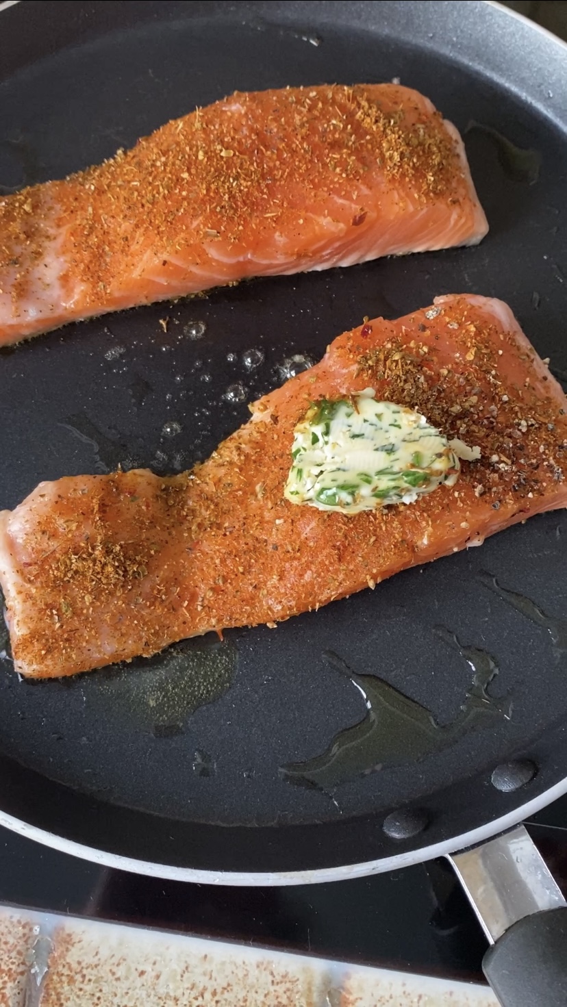 Slice of herb butter added on the salmon fillets, in the frying pan.