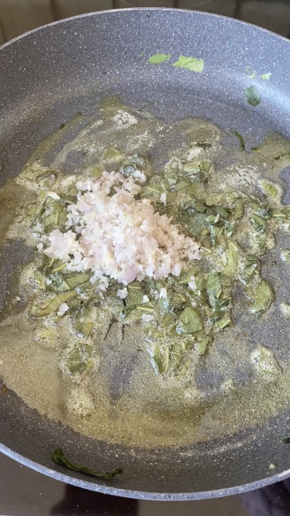 Échalote émincée ajoutée à la poêle avec du beurre fondu et des feuilles de sauge hachées.