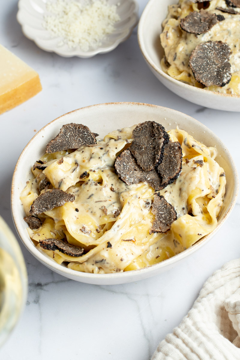 Creamy truffle pasta with truffle slices in a beige bowl. 