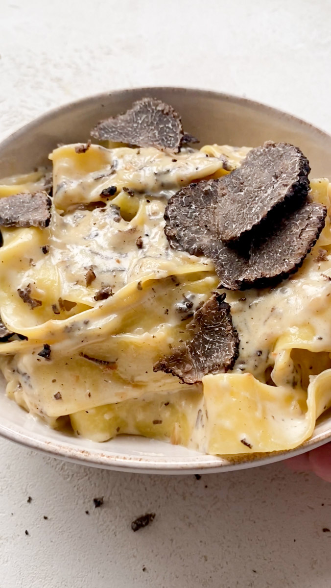 Creamy black truffle pasta dish ready to be served, in a beige bowl.