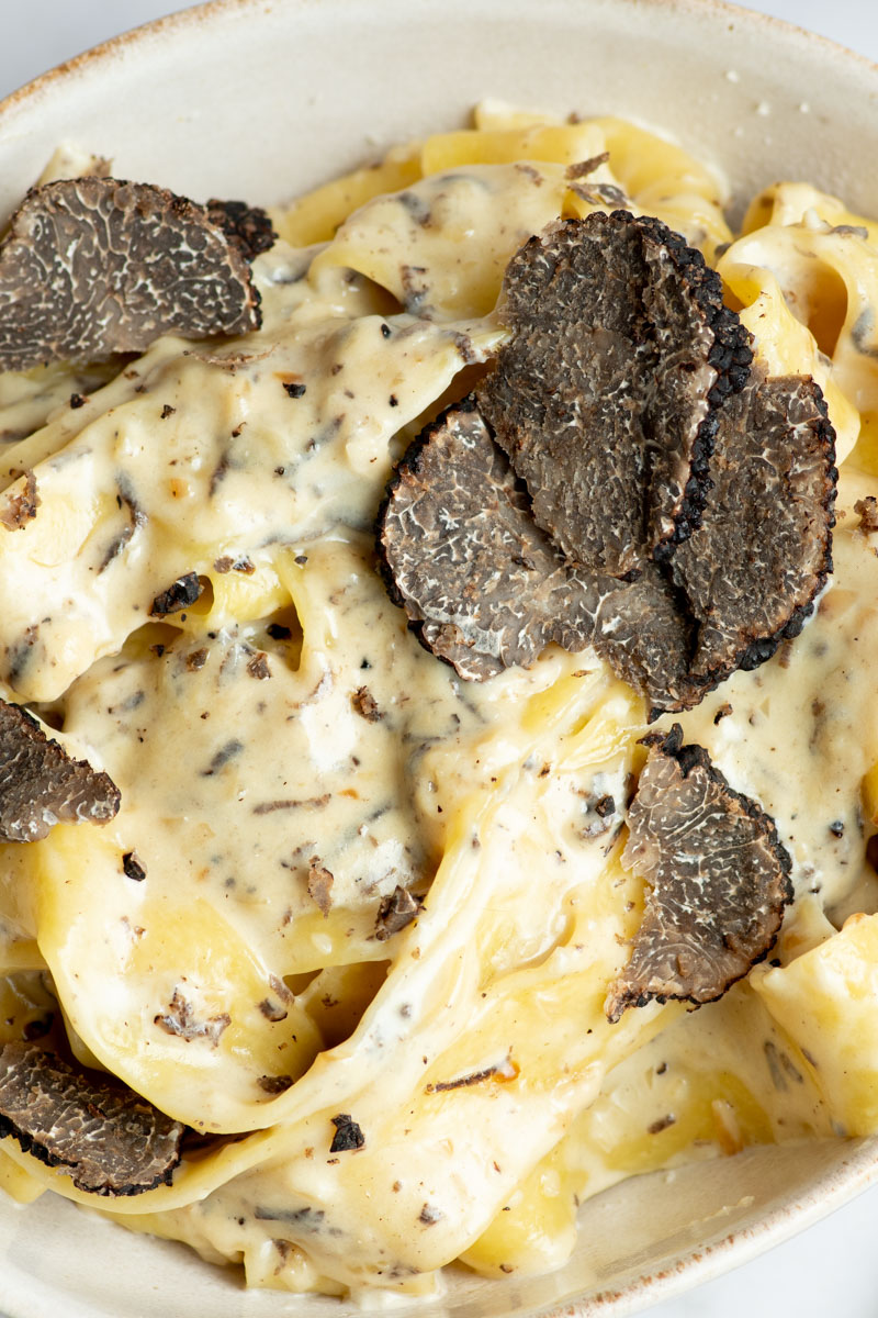 Creamy truffle pasta with truffle slices in a beige bowl.