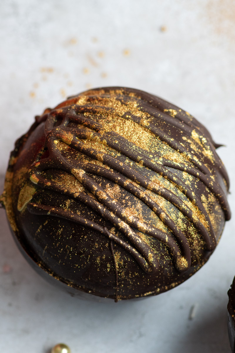 A hot chocolate bomb sprinkled with gold edible glitter.