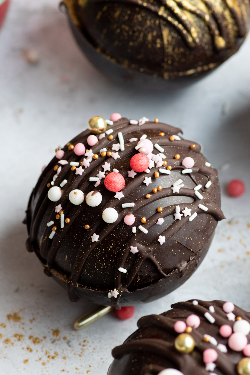 A hot chocolate bomb sprinkled with pink sprinkles.