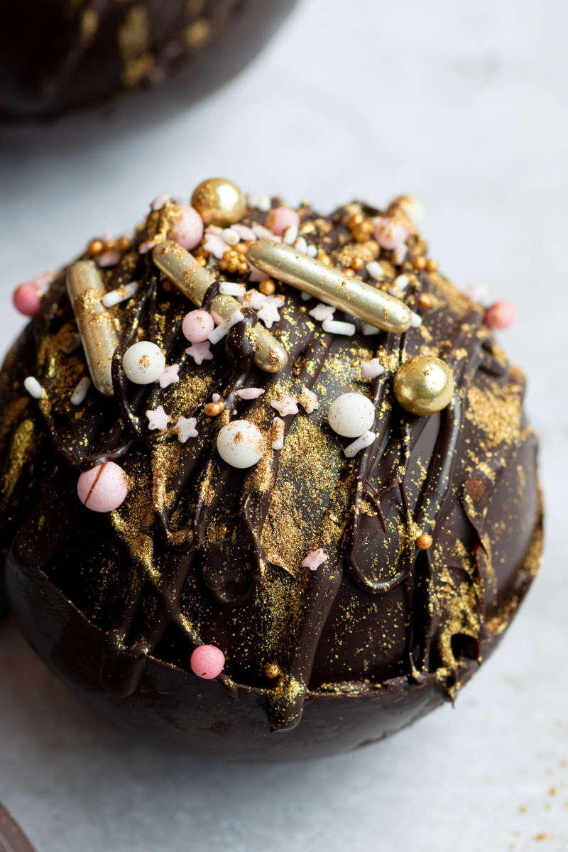 A hot chocolate bomb with gold edible glitters and sprinkles.
