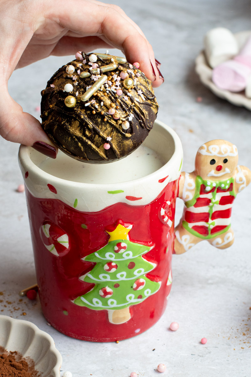 Une main mettant une bombe de chocolat chaud dans une tasse de Noël avec du lait.