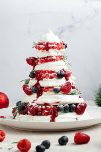 Pavlova de Noël dans une assiette blanche avec des fruits rouges, une boule de Noël et une couronne de sapin.