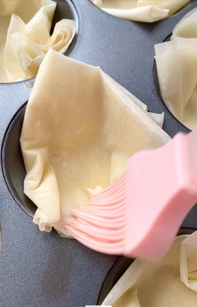 Feuille filo dans un moule à muffin, badigeonnée de beurre par un pinceau en silicone rose.