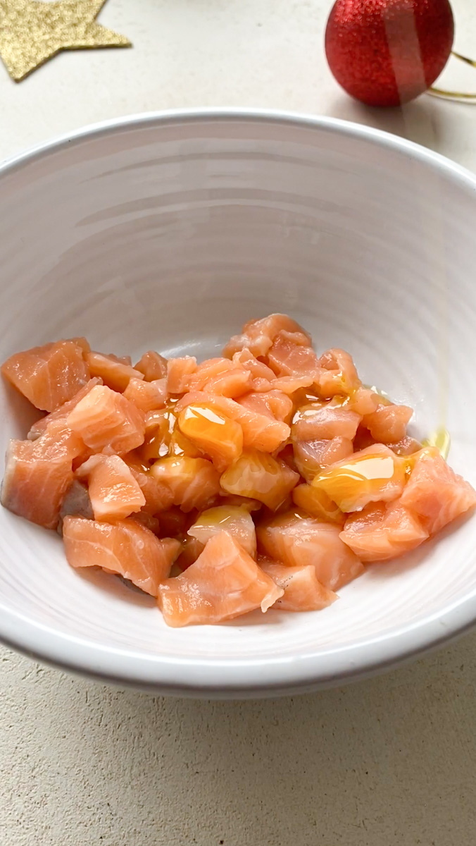 Huile d'olive qui tombent sur les cubes de saumon, placés dans un bol blanc.