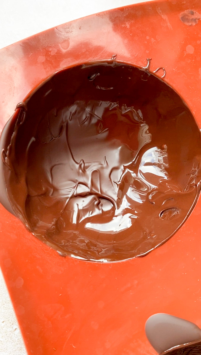 Deuxième couche de chocolat fondu ajoutée au moule marron en forme de demi-sphère.