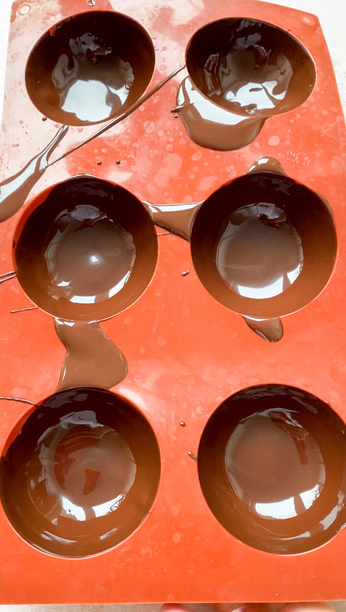 Melted chocolate in brown silicone half-sphere molds.