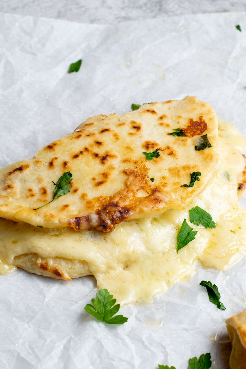 Naan façon Grilled Cheese avec du fromage fondant et du persil frais sur papier sulfurisé.