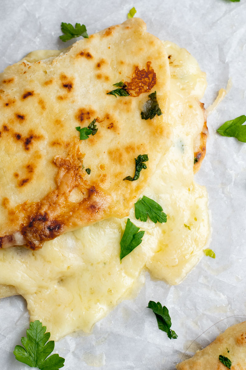 Garlic Naan Grilled Cheese with melting cheese and fresh parsley on parchment paper.