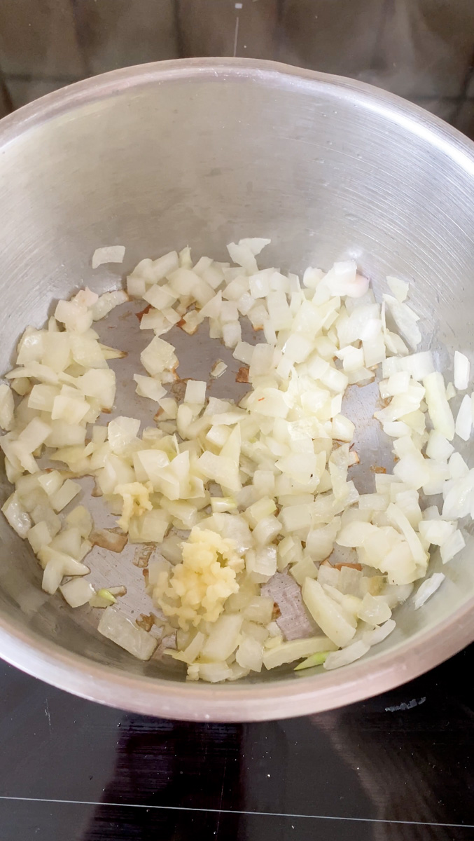 Thinly chopped onion and minced garlic cooking in a saucepan.