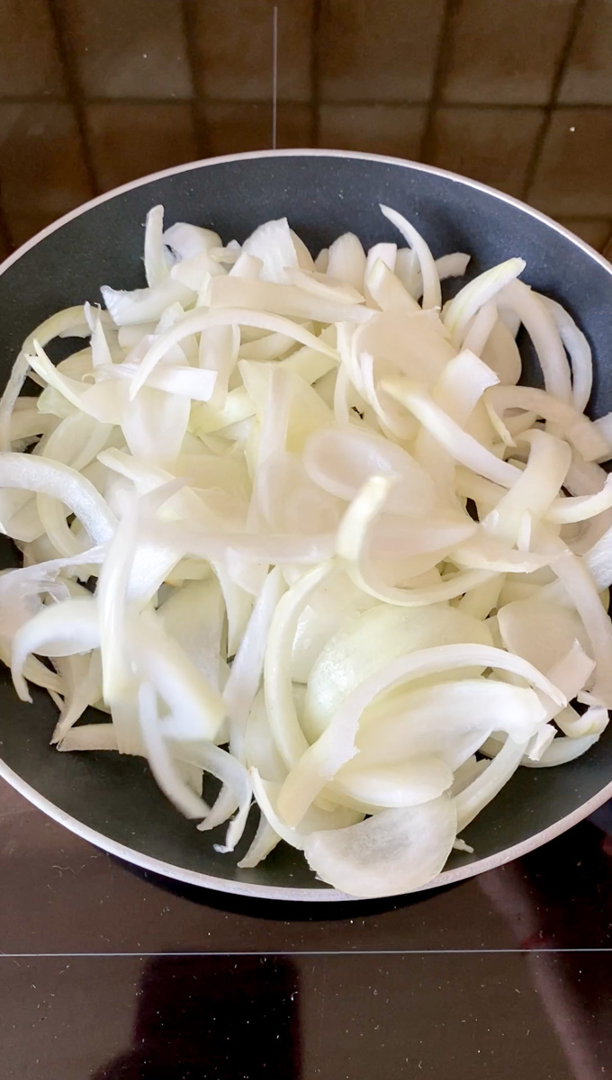 Onion strips in a black frying pan.