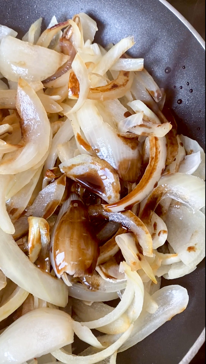 Onion strips in a black frying pan with Balsamic vinegar.