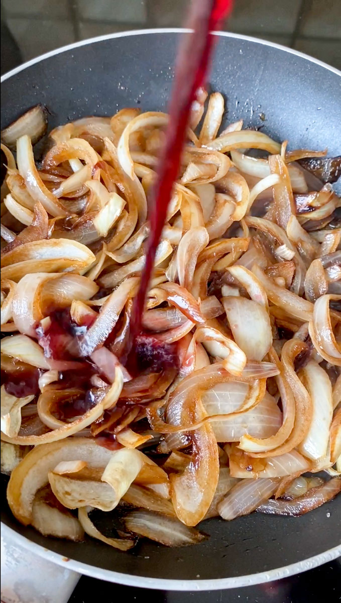 Onion strips in a black frying pan with red wine.