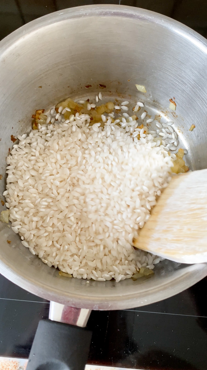 Risotto rice added to the saucepan with a wooden spoon.