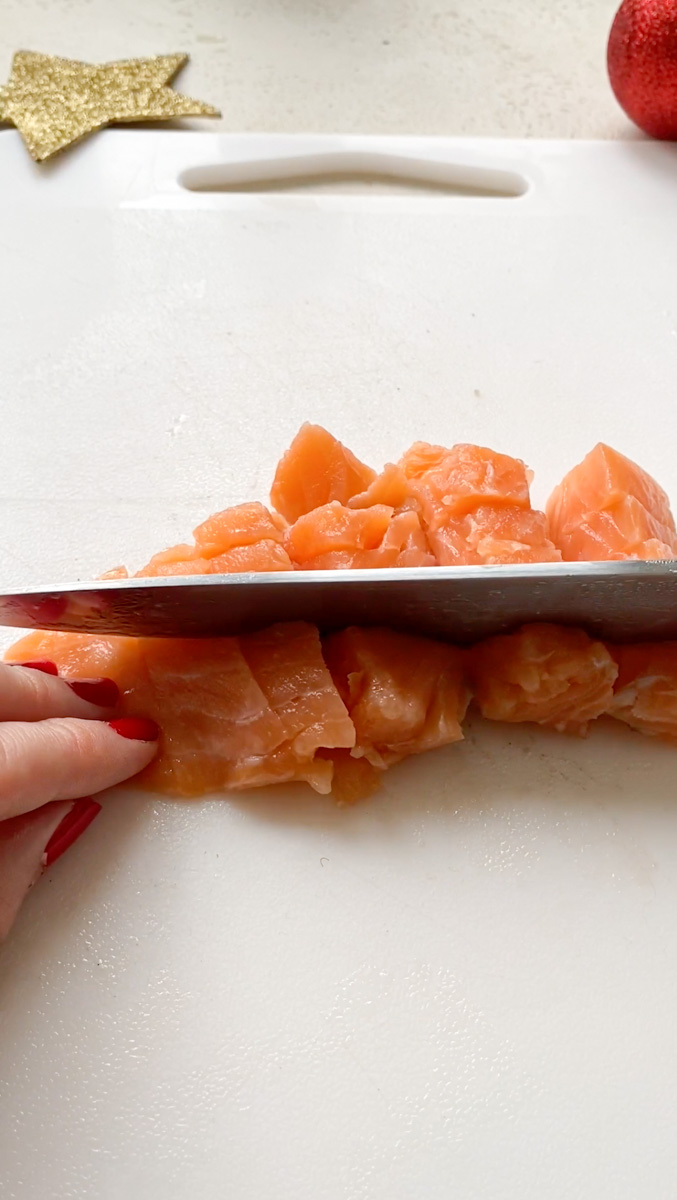 Une main qui tient des cubes de saumon pendant qu'un couteau les découpe.