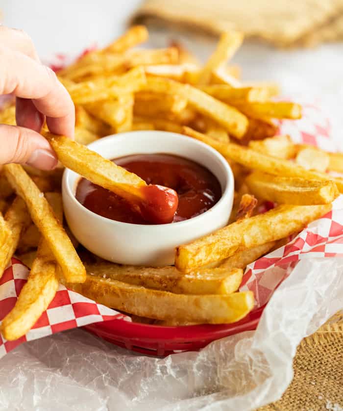A hand holding a French fries and dips it in the sauce.