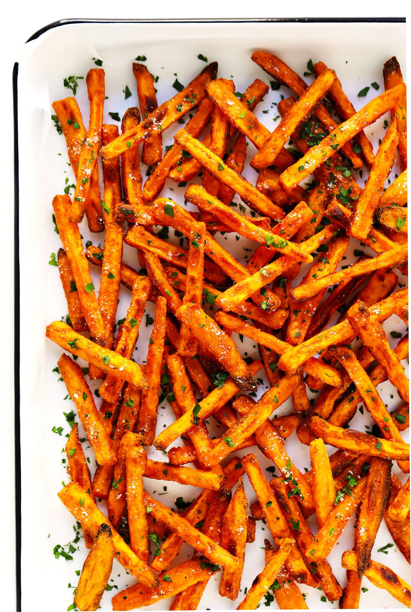 Sweet potato fries in a white baking dish, with fresh chopped parsley.