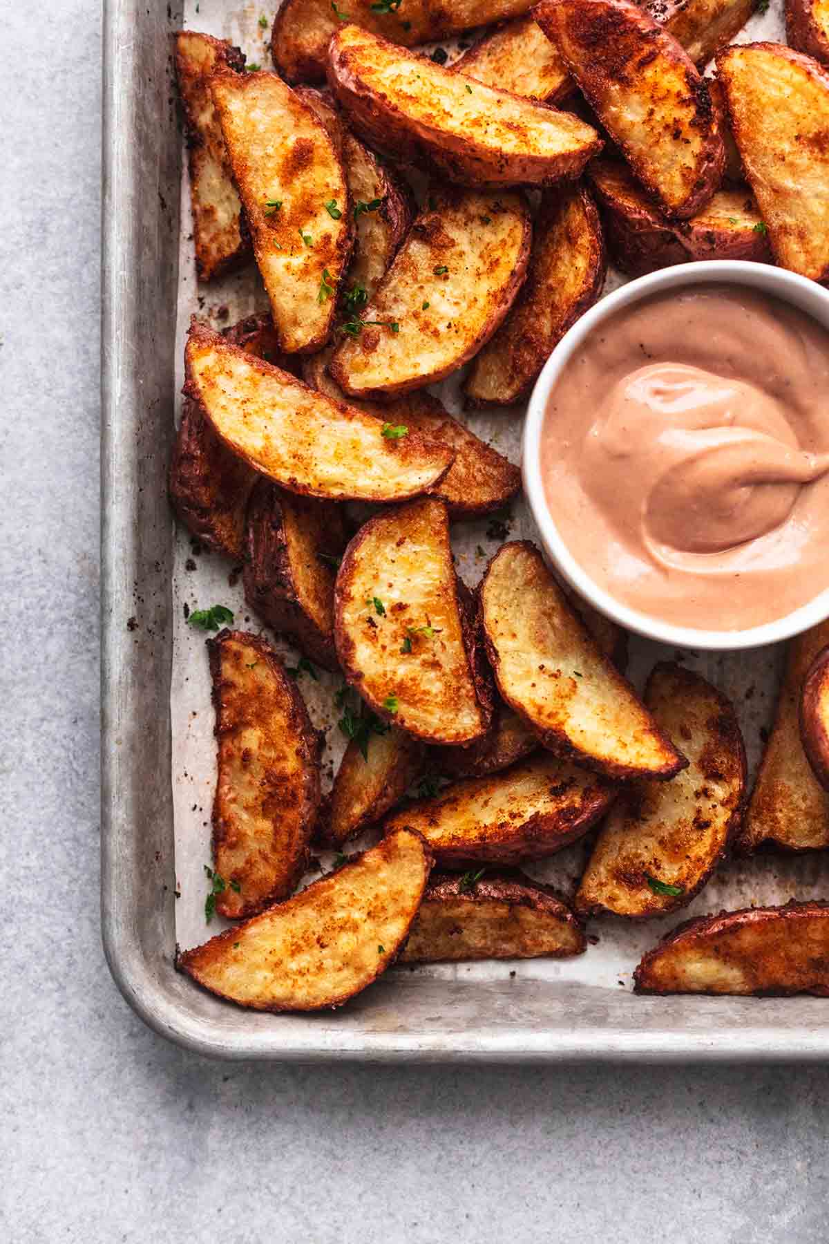 Potato wedges on a baking tray with a small bowl of pink sauce.