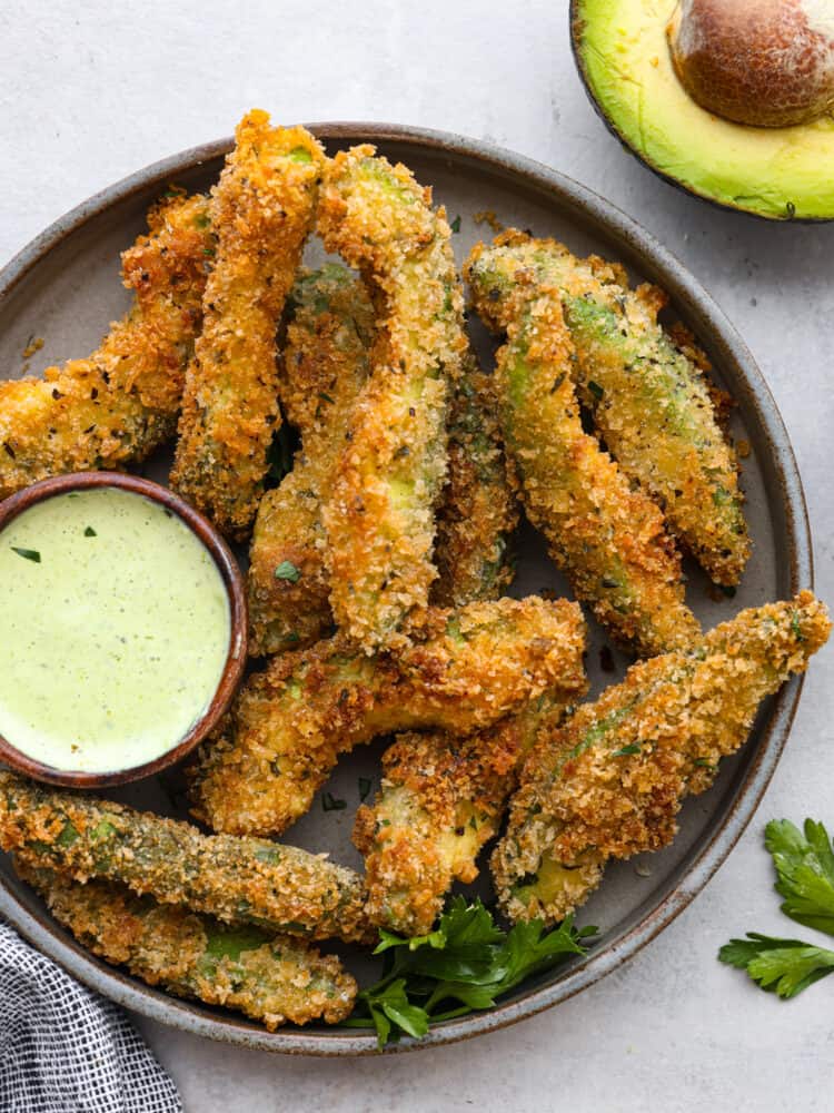 Avocado fries in a dark grey plate with a small bowl of green sauce.