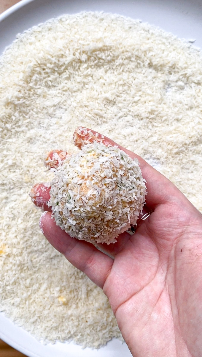 A hand holding a sweet potato ball coated with Panko breadcrumbs.