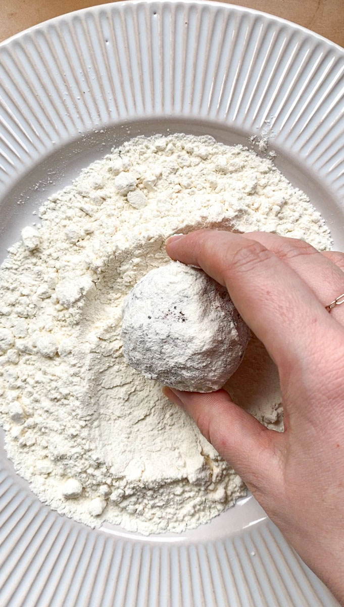A hand coating a sweet potato ball in a white plate, filled with flour.