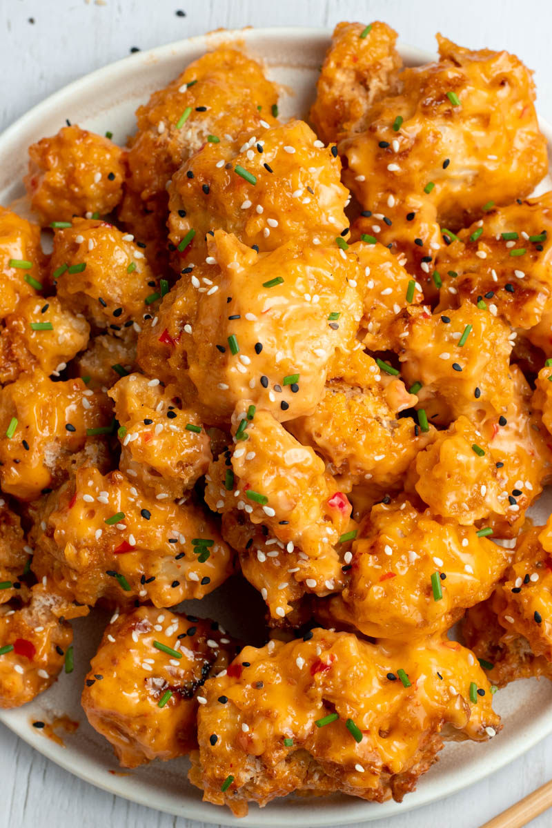 Bang Bang cauliflower with sesame seeds and fresh chopped chives in a white plate.