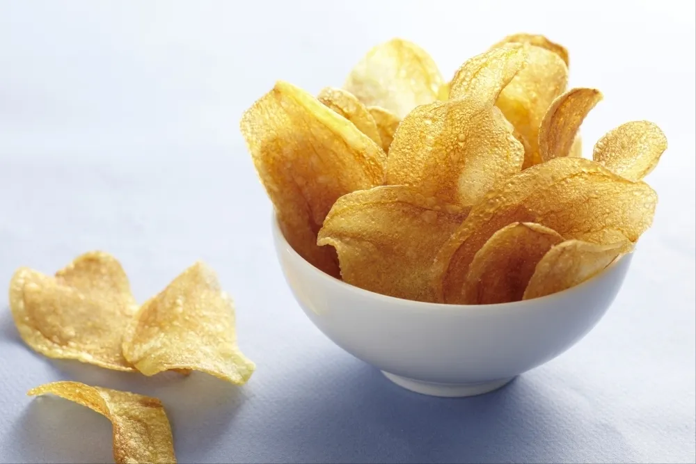 Chips de pommes de terre maison dans un bol blanc sur un plan de de travail gris/bleu.