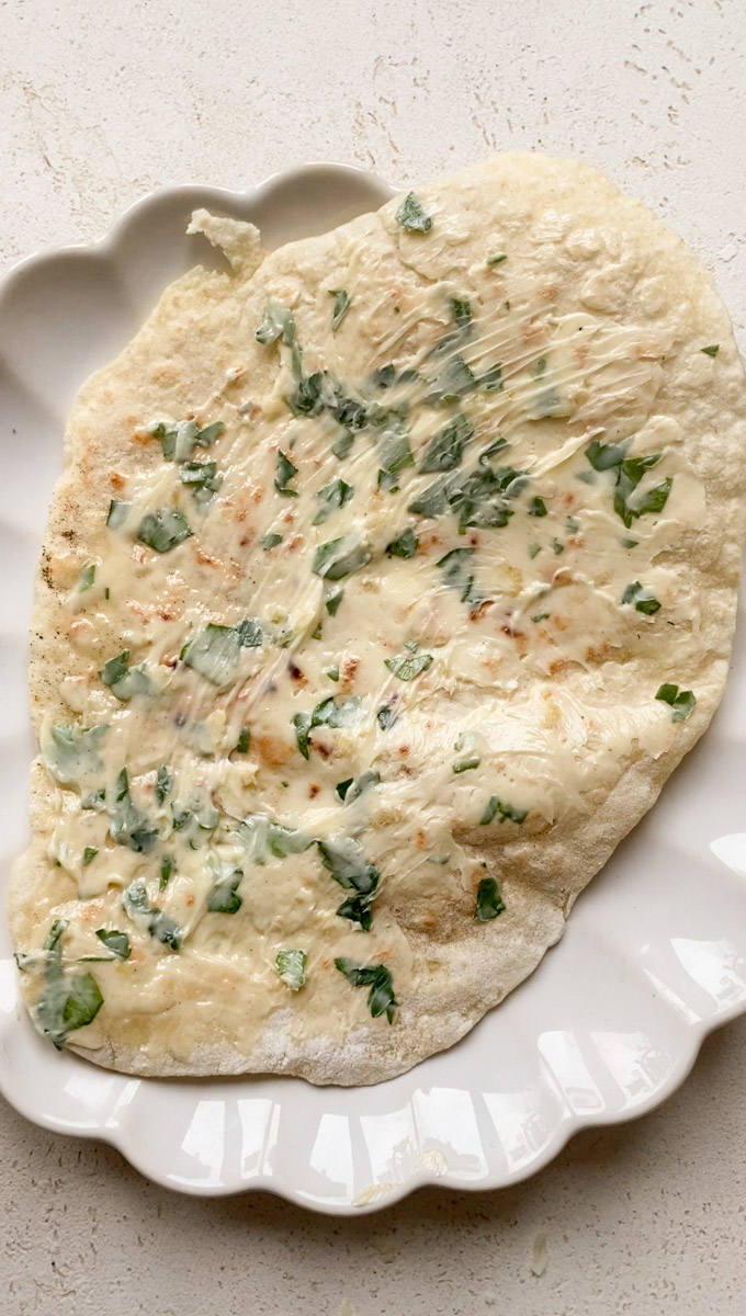 Naan spread with garlic and parsley butter in a white plate.