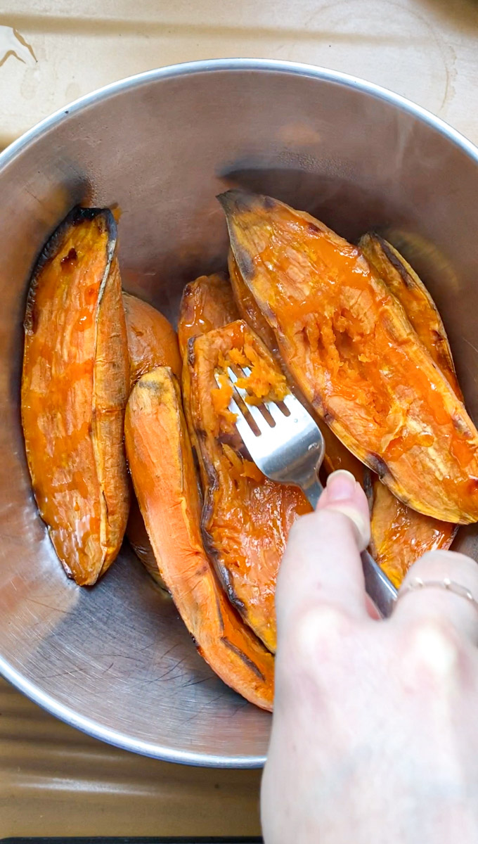 A hand holding a fork and crushing the cooked sweet potatoes.