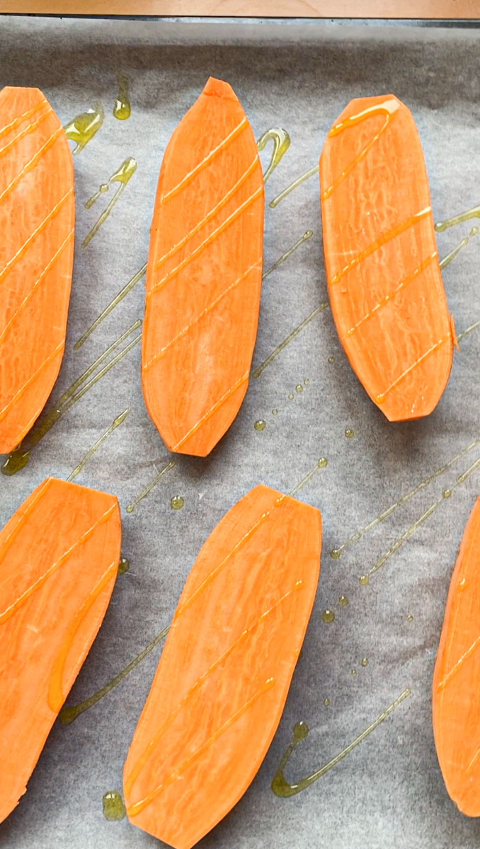 Halves of sweet potato placed on parchment paper on a baking tray and drizzled with olive oil.